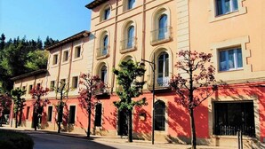 A multi-story building with arched windows and balconies, surrounded by trees and a cobblestone street. - Hostal Montsoliu (Arbucies)