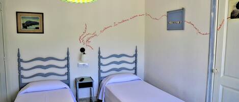 A room with two beds, a nightstand, a lamp, and a framed picture on the wall.