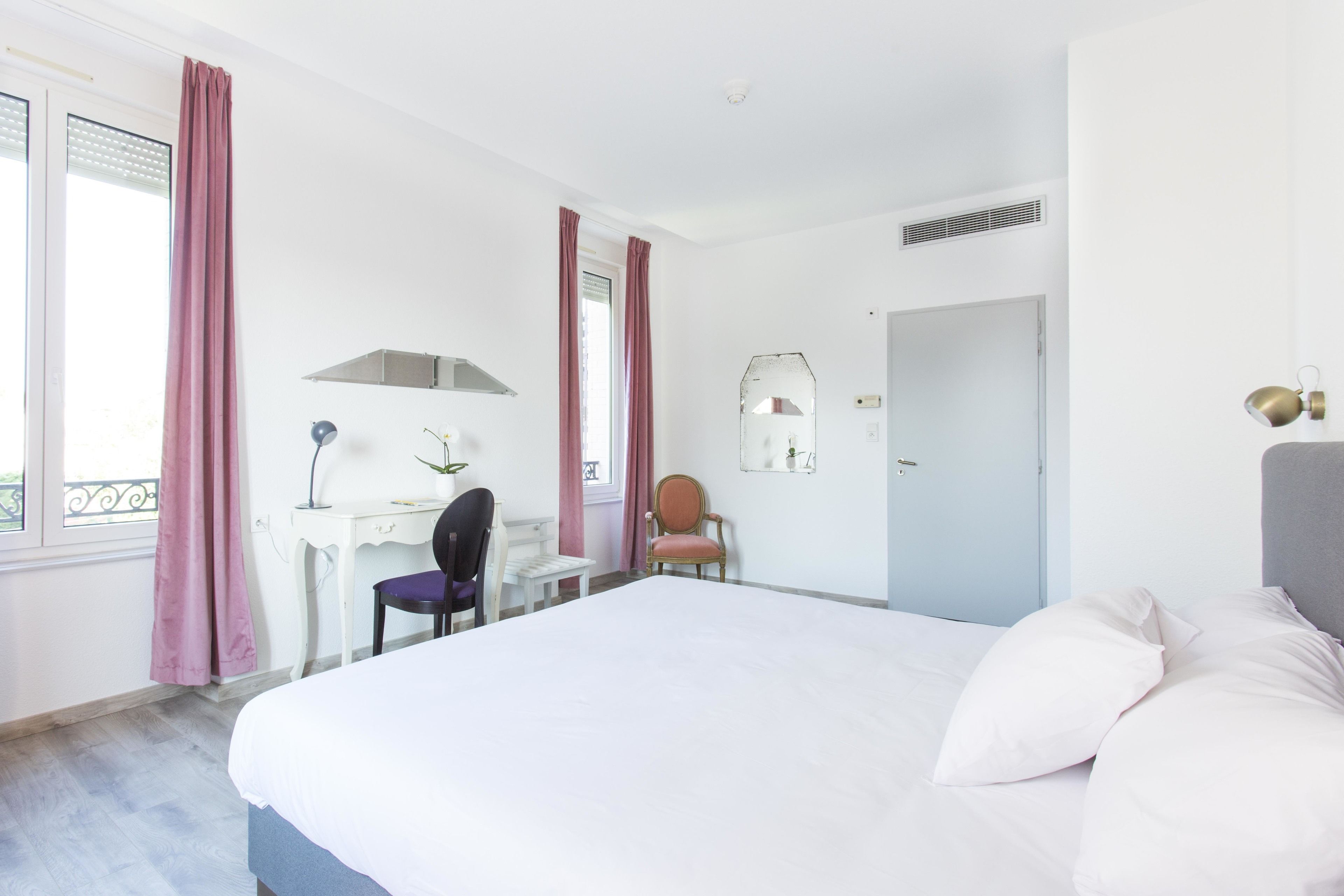 Una habitación de hotel con cama, escritorio, silla, espejo y puerta.
