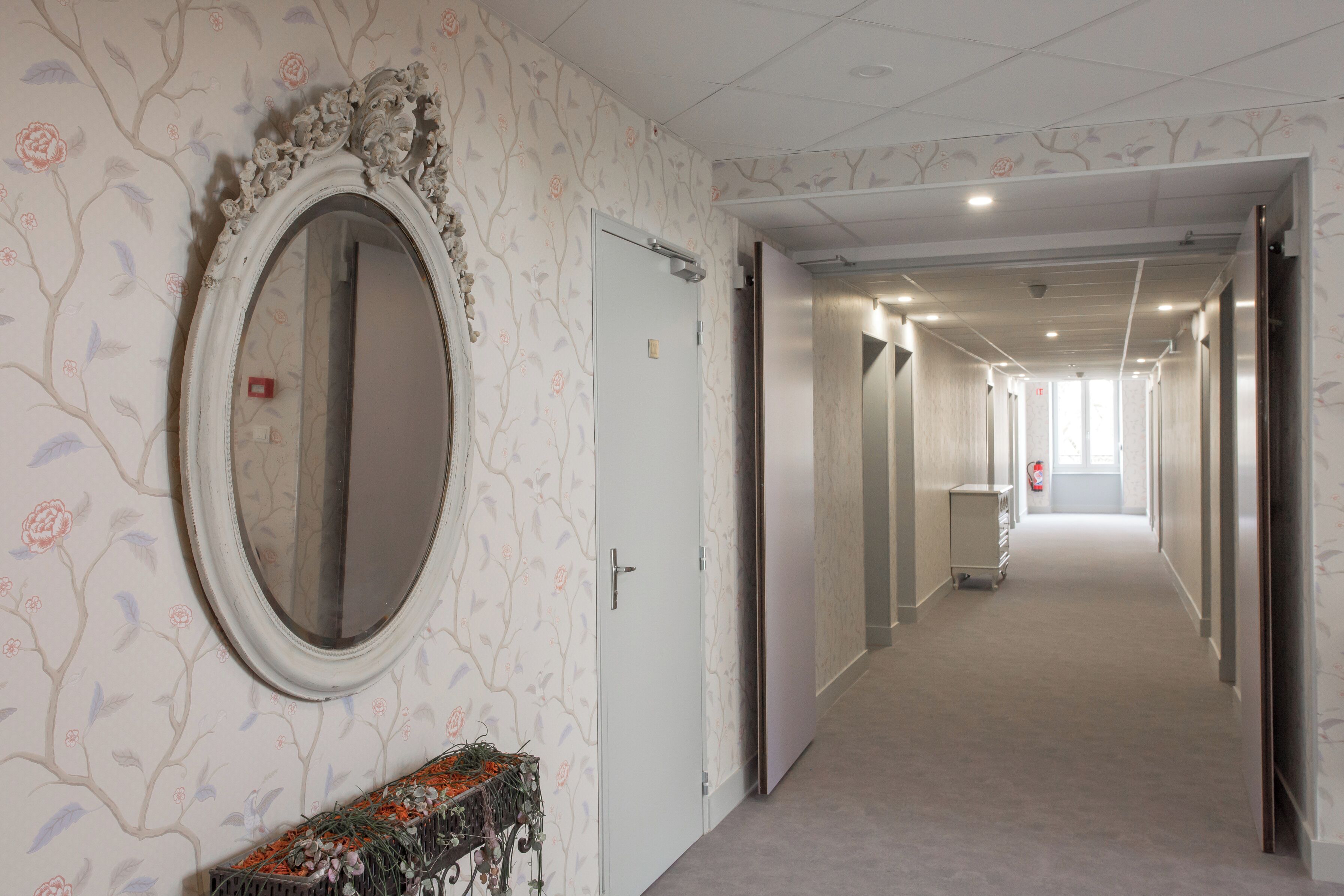 A hallway with floral wallpaper, a large mirror, and doors leading to other rooms.