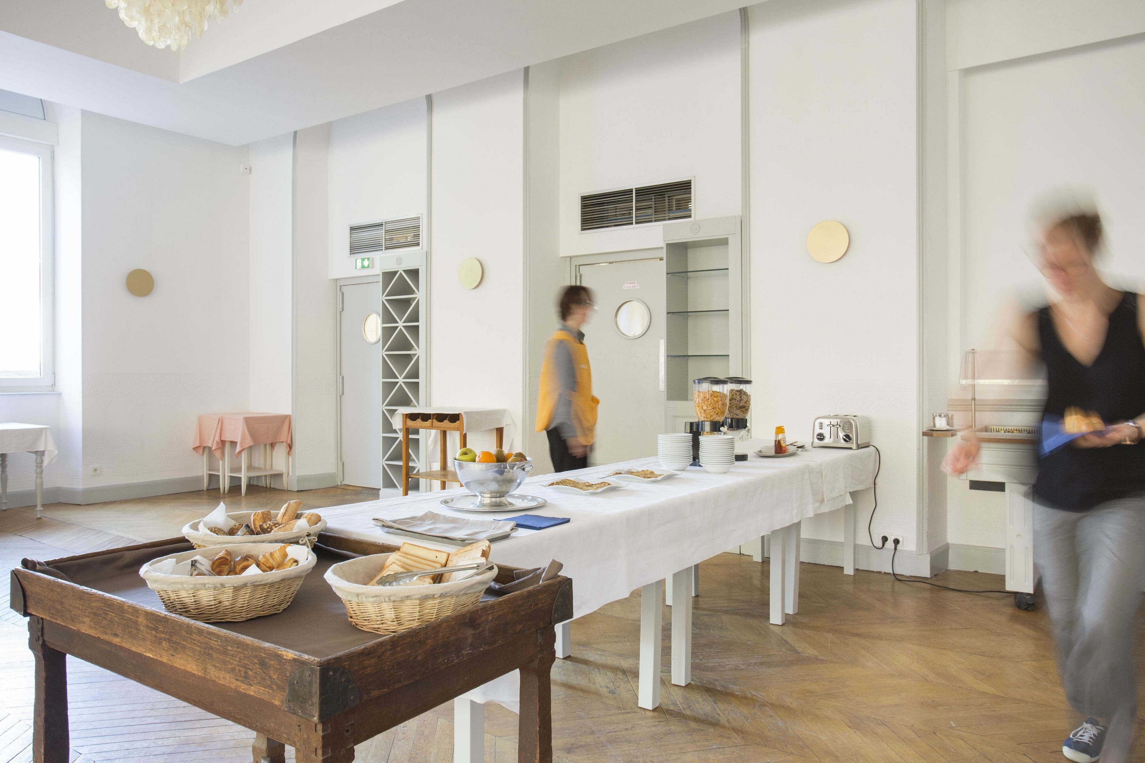 Une pièce avec une longue table dressée pour un repas, des paniers de pain et une personne qui marche.