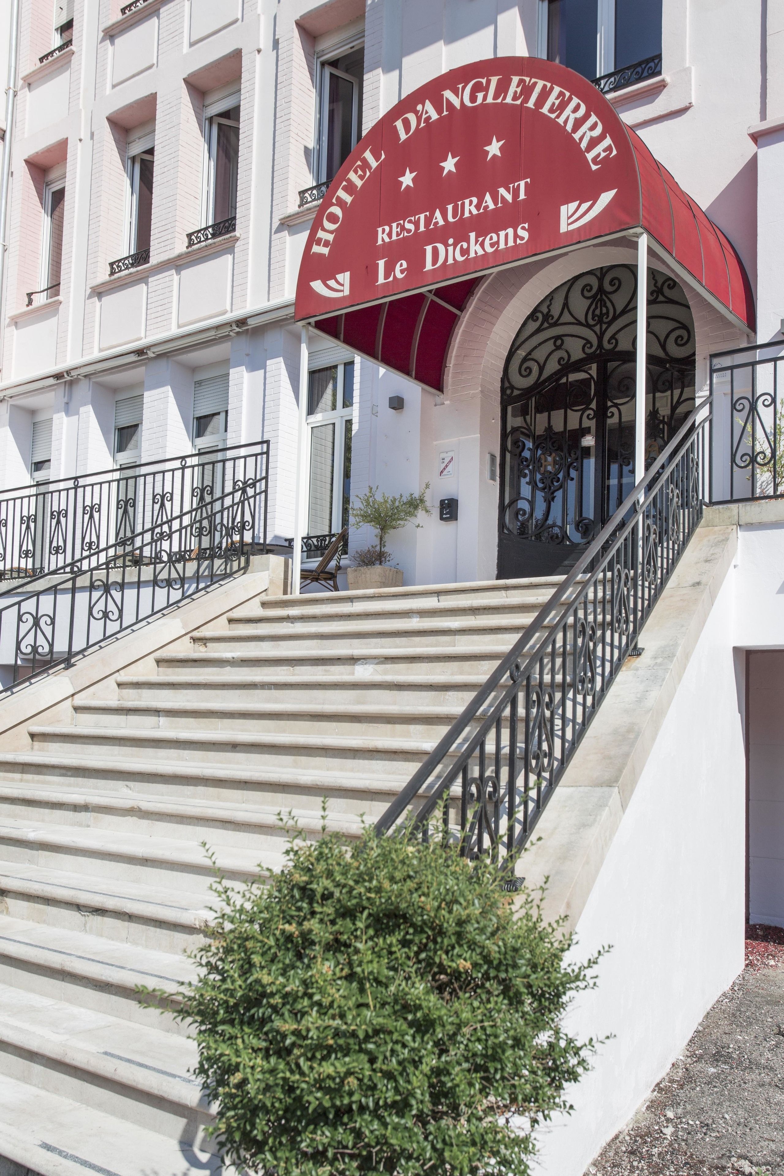 A hotel entrance with a red awning, a staircase, and a small potted plant.