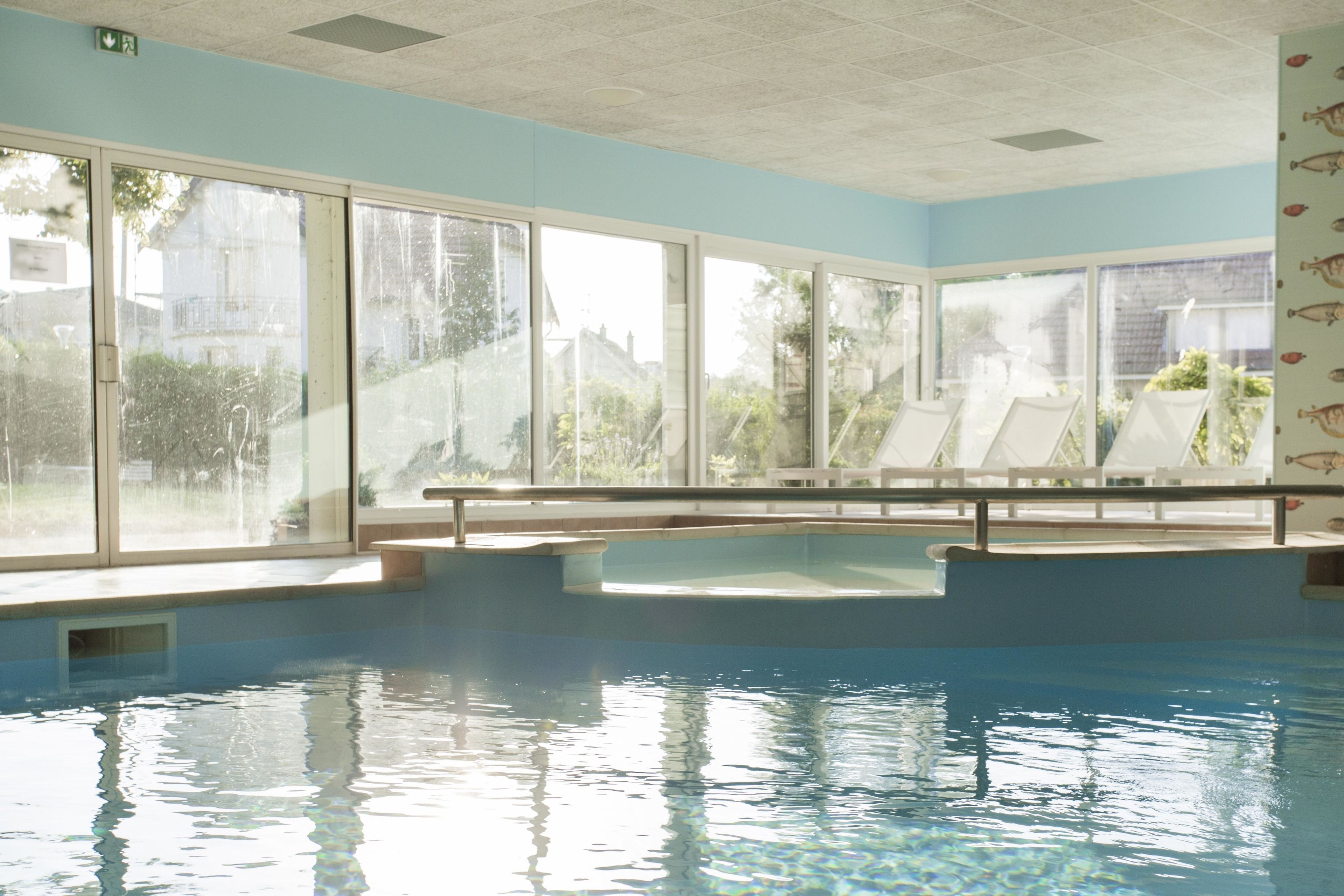 Una piscina interior con amplios ventanales de vidrio, revestimiento azul y vistas al exterior.