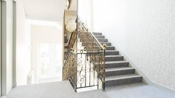 A staircase with ornate black railings and a chandelier, leading to a door with a view of greenery outside.