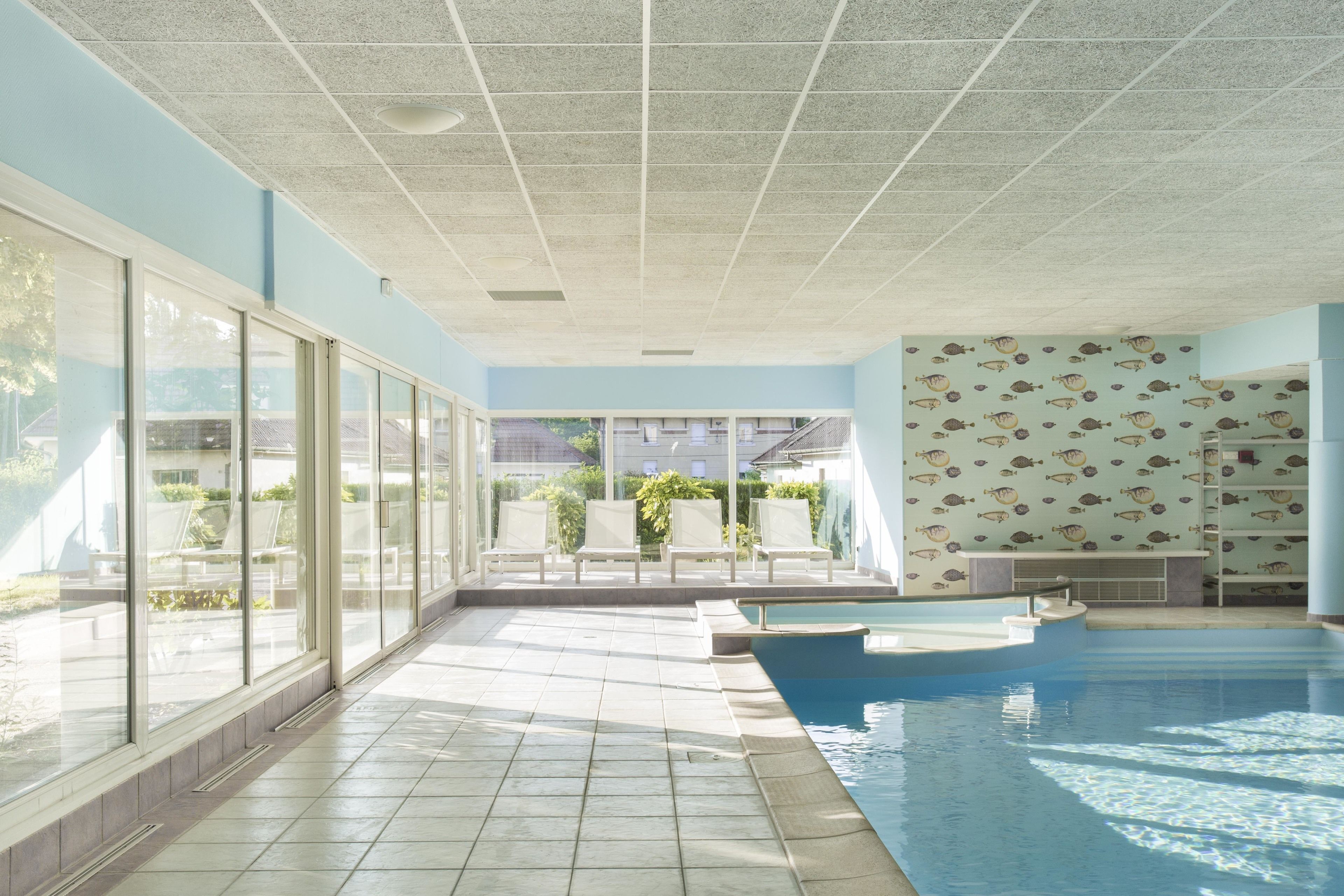 Una piscina interior con paredes de vidrio transparente, suelo de baldosas y techo con diseño de cuadrícula.