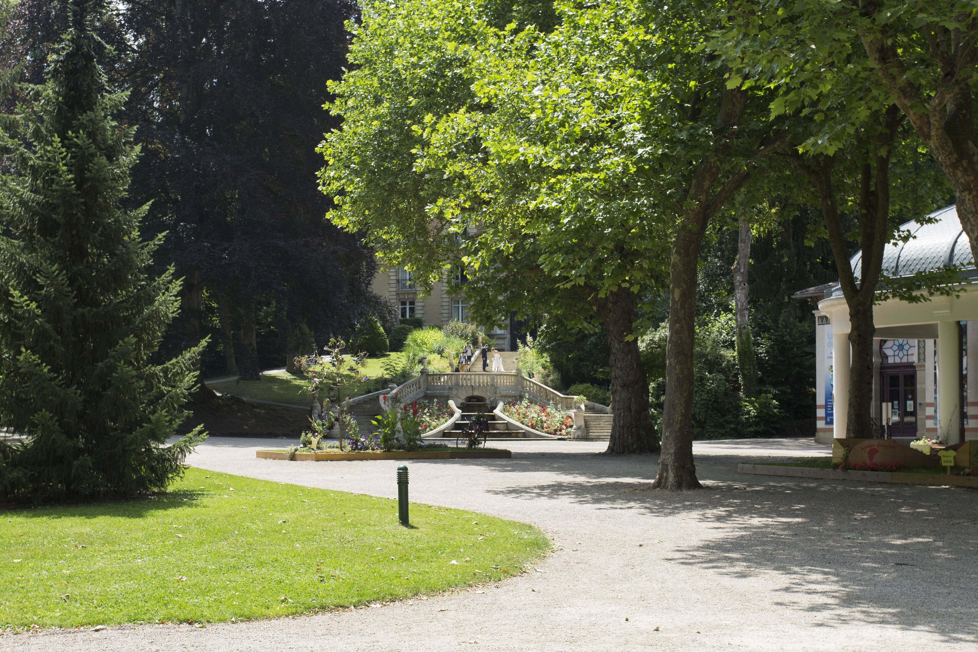 Un parque con un puente de piedra, árboles y un edificio con columnas.
