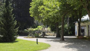 Un parque con un puente de piedra, árboles y un edificio con columnas.