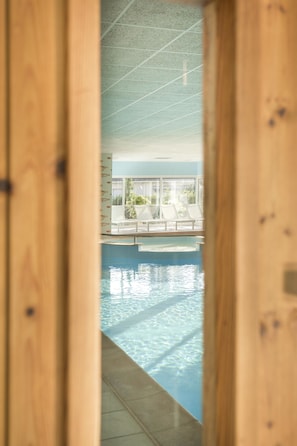 Vista attraverso una porta in legno su un'area piscina con sedie a sdraio e affaccio sull'esterno.