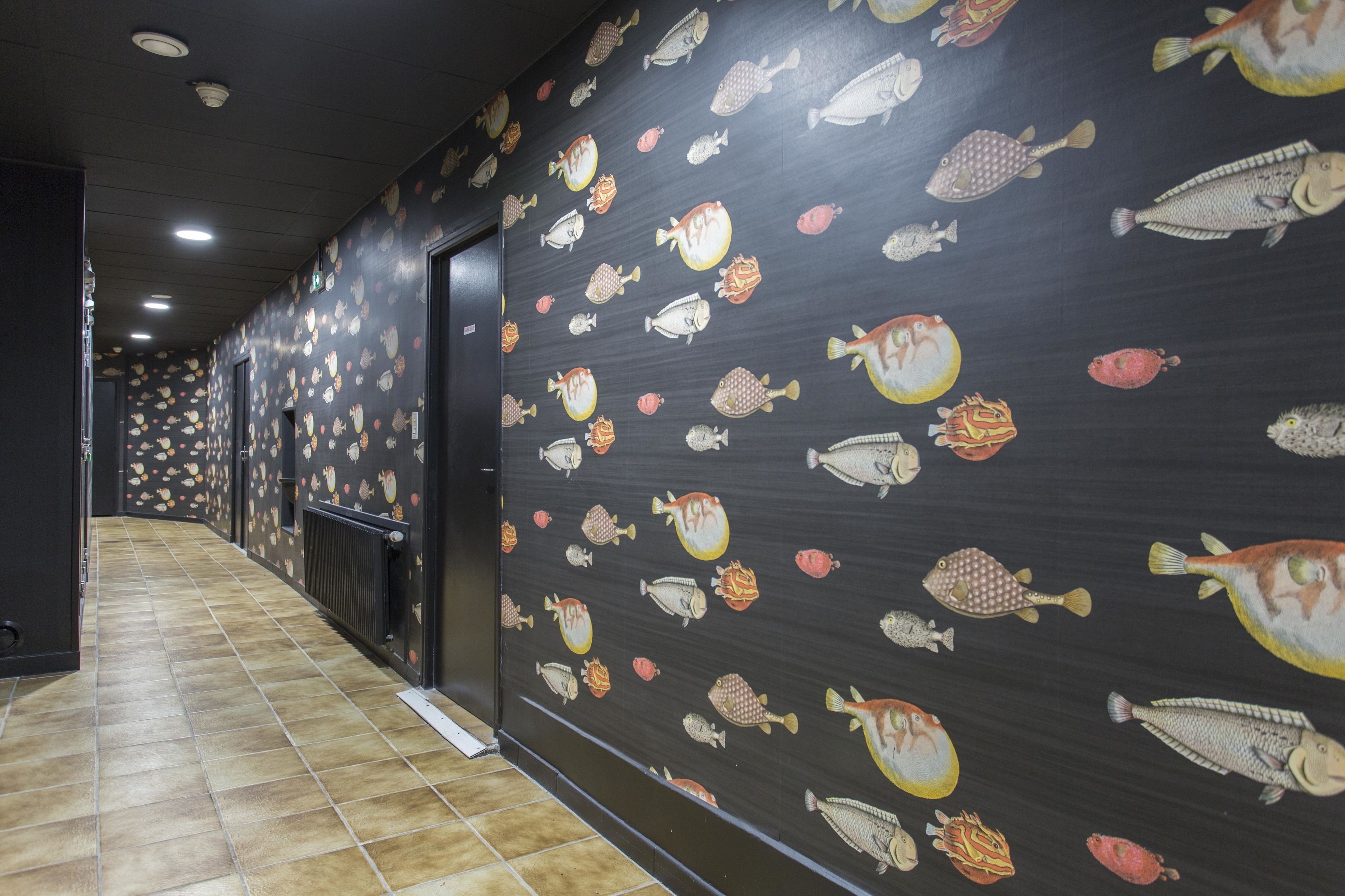 Un couloir doté d’un sol carrelé et de murs décorés de motifs représentant des poissons.