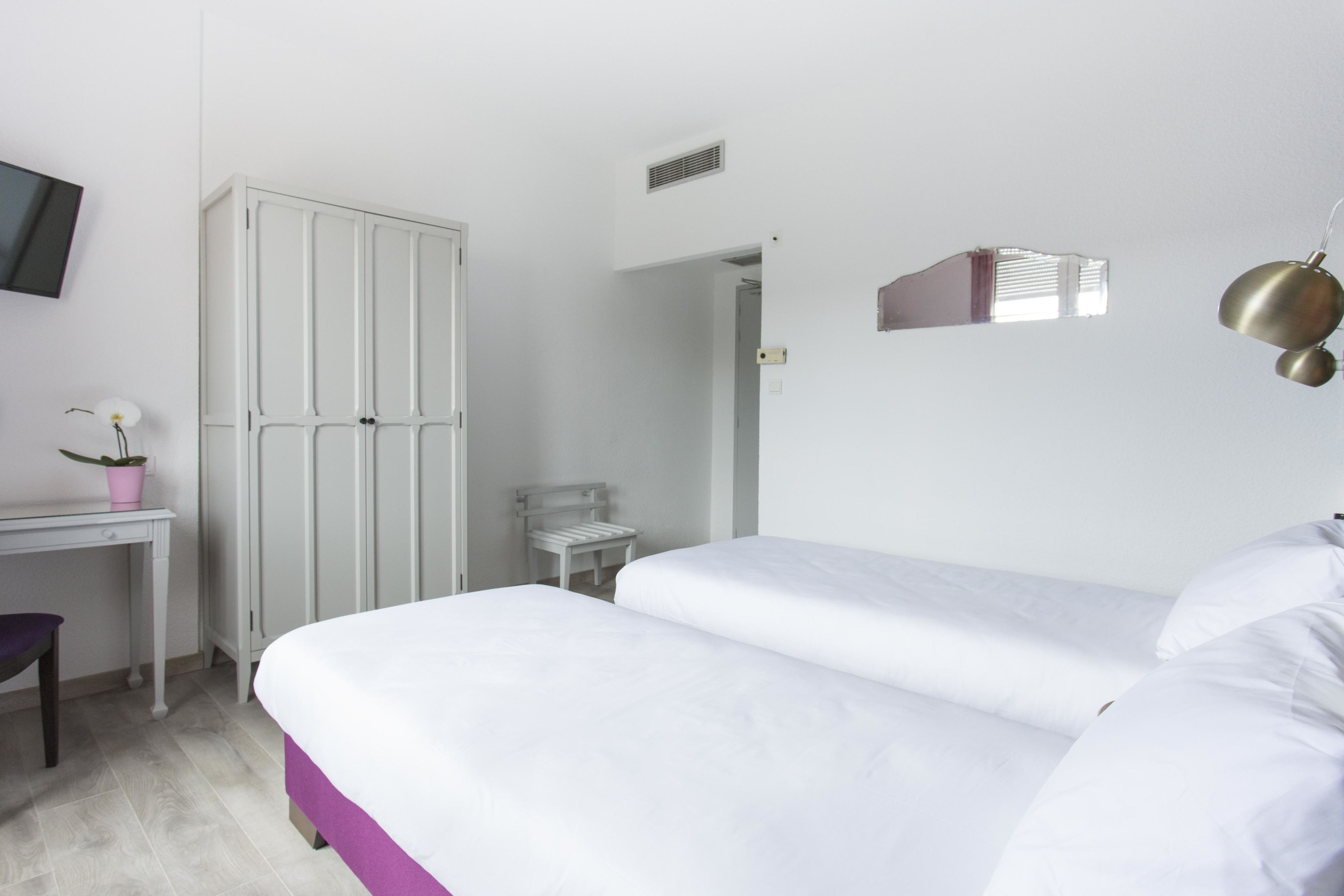 A bedroom with a bed, a desk, a chair, a wardrobe, and a small table with a potted plant.