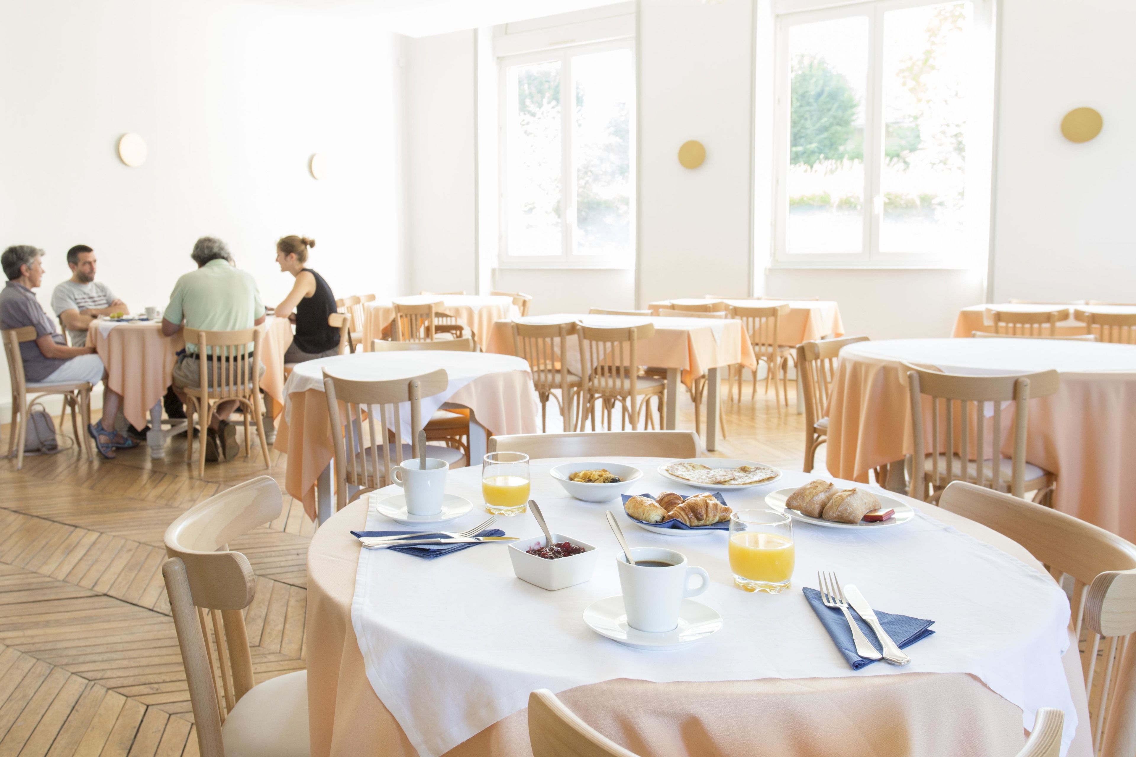 Un espace repas avec des tables rondes, des chaises et des produits pour le petit-déjeuner, comme des croissants et du jus d’orange.