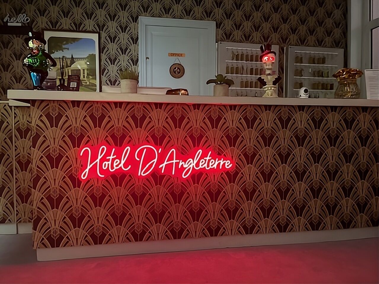 A reception desk with a neon sign reading "Hotel D'Angleterre" and a patterned wallpaper background.