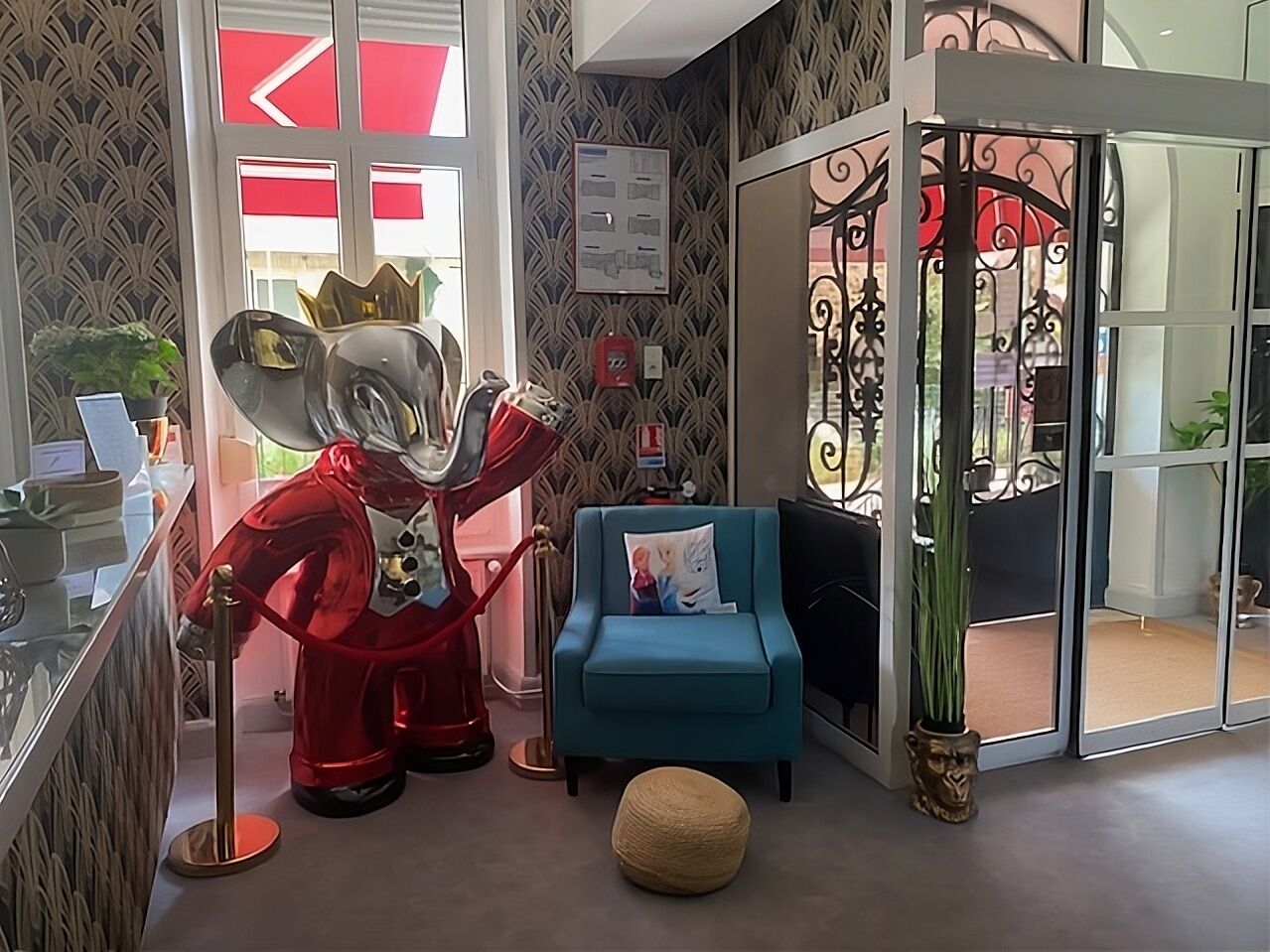 Un salón moderno con un sillón azul, una escultura roja y un separador de vidrio.