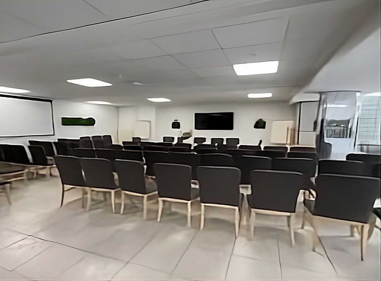 A conference room with rows of chairs, a projector screen, and a flat-screen TV on the wall.