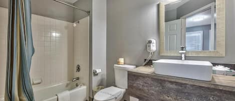 Un baño con bañera, inodoro y tocador con espejo.