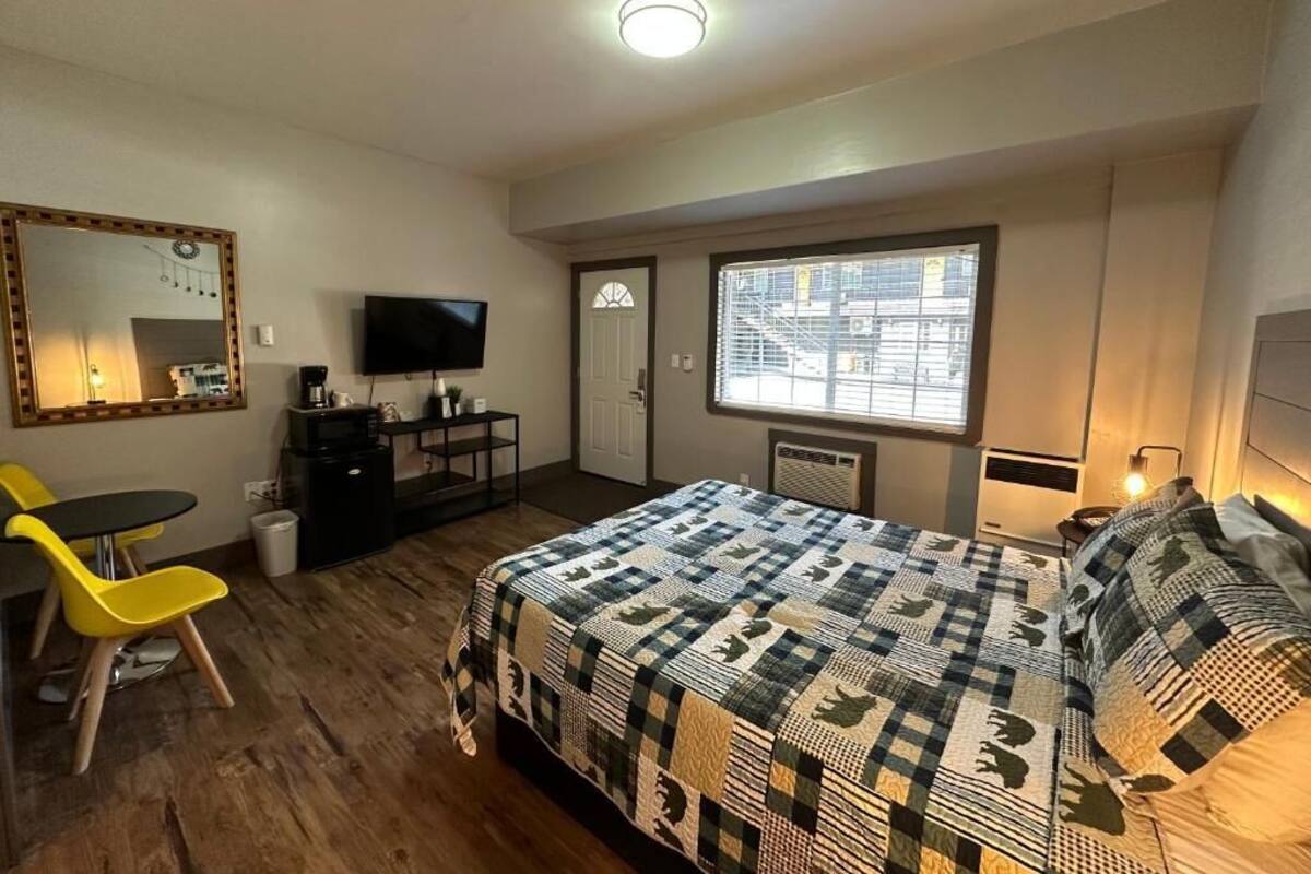 Une chambre à coucher comprenant un lit, un bureau, une chaise, un téléviseur et une fenêtre donnant sur des immeubles.
