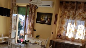 A dining area with a table set for four, surrounded by white chairs with cushioned seats. An air conditioning unit is mounted on the wall above the table. - B&B Dolce Casa (Castiglione del Lago)