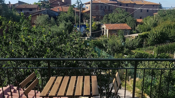 A terrace with a table and chairs, surrounded by greenery and a view of a town with a clock tower. - B&B Dolce Casa (Castiglione del Lago)
