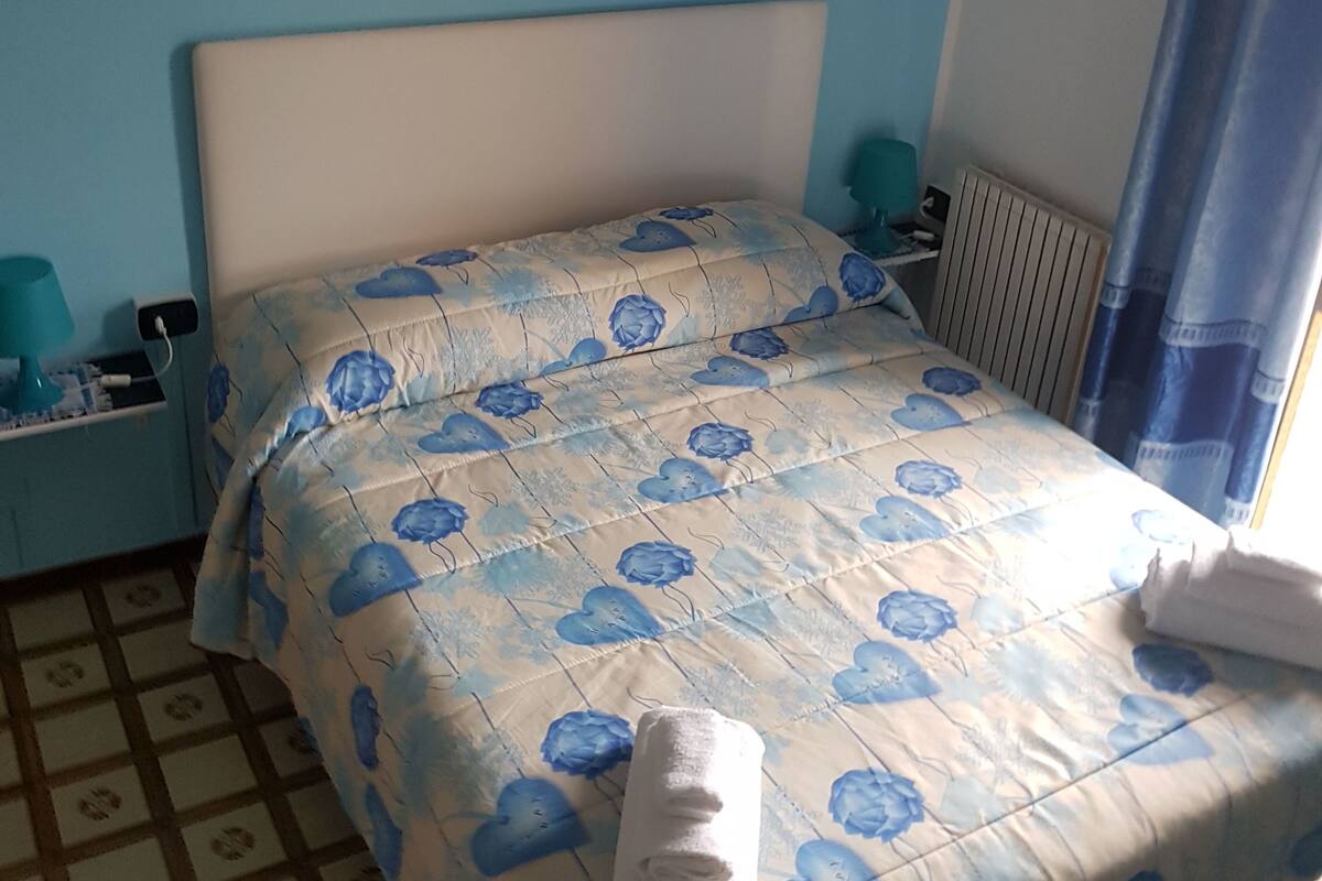A bedroom with a bed, a nightstand, a lamp, a radiator, and a painting on the wall.