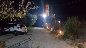A nighttime view of a road leading to a church with a bell tower, surrounded by trees and a parked car. - B&B Dolce Casa (Castiglione del Lago)