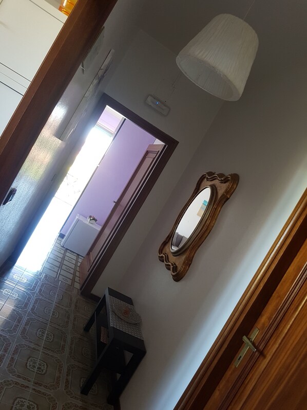 A hallway with a patterned floor, a mirror, and a ceiling light fixture. - B&B Dolce Casa (Castiglione del Lago)