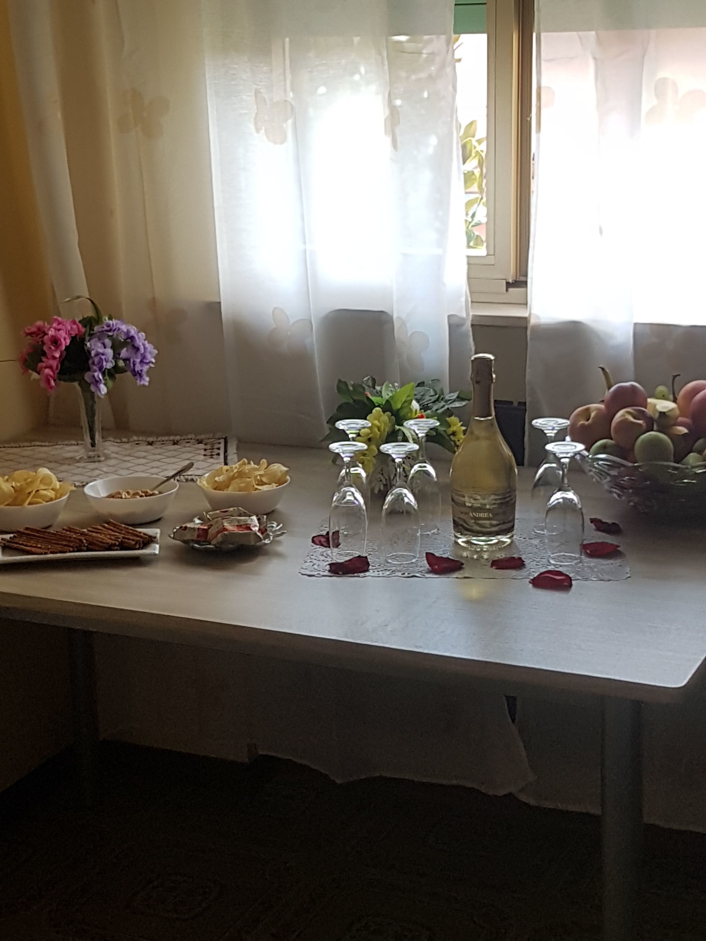 A dining table with a bottle, glasses, and a bowl of fruit.