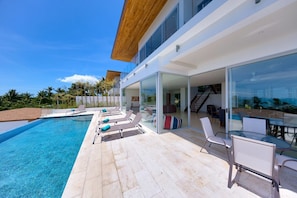 A modern house with a swimming pool, outdoor seating, and a glass-enclosed patio.