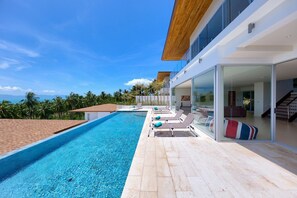 Una casa moderna con piscina, sillones de descanso y vista al océano.