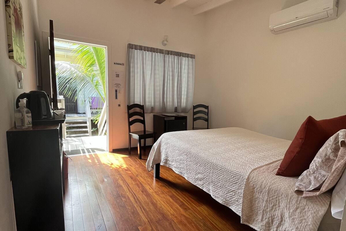 A bedroom with a bed, a desk, a chair, a ceiling fan, and a view of the outdoors.