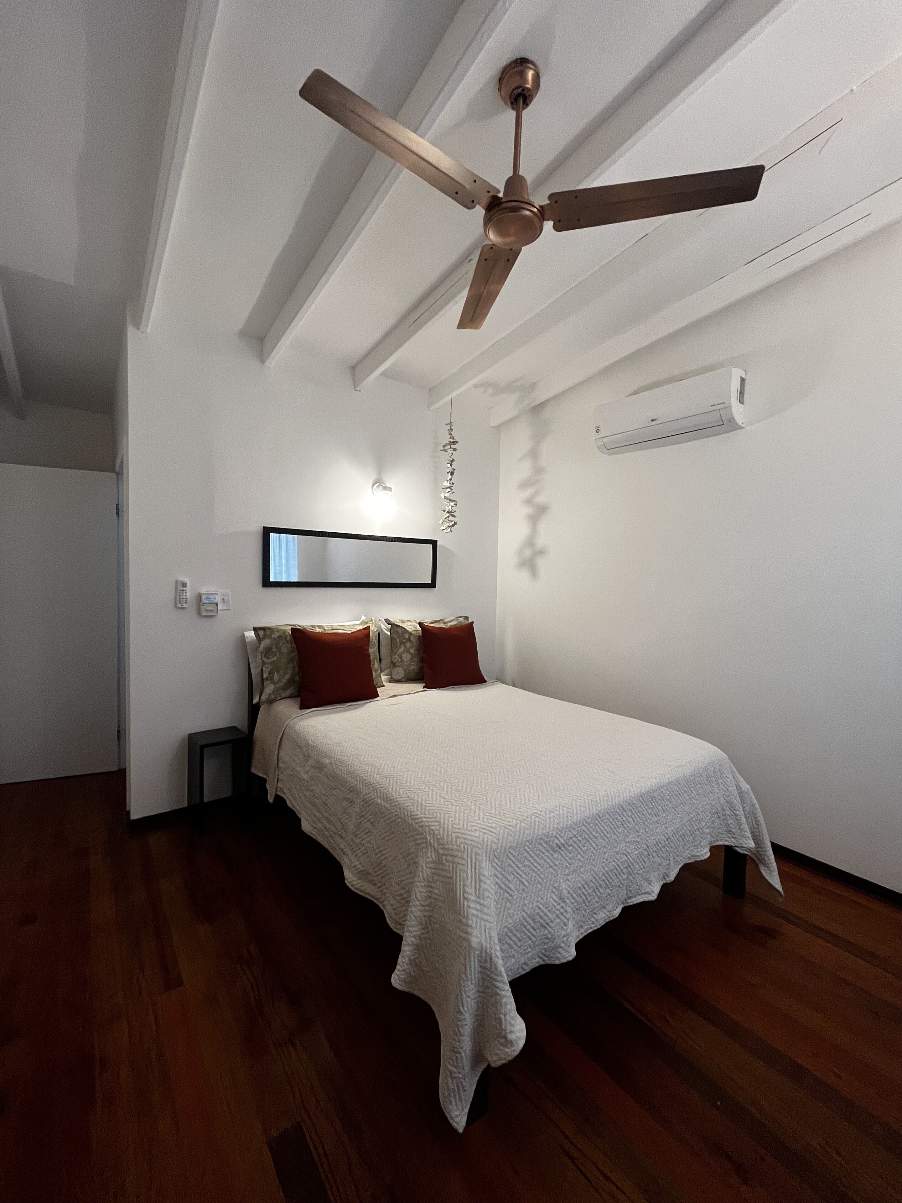 A bedroom with a bed, a ceiling fan, an air conditioning unit, and a wall-mounted TV.