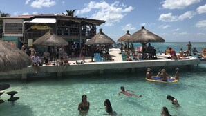 En badehotel med poolområde, stråtækte parasoller og en restaurant kaldet 'Landshark'.