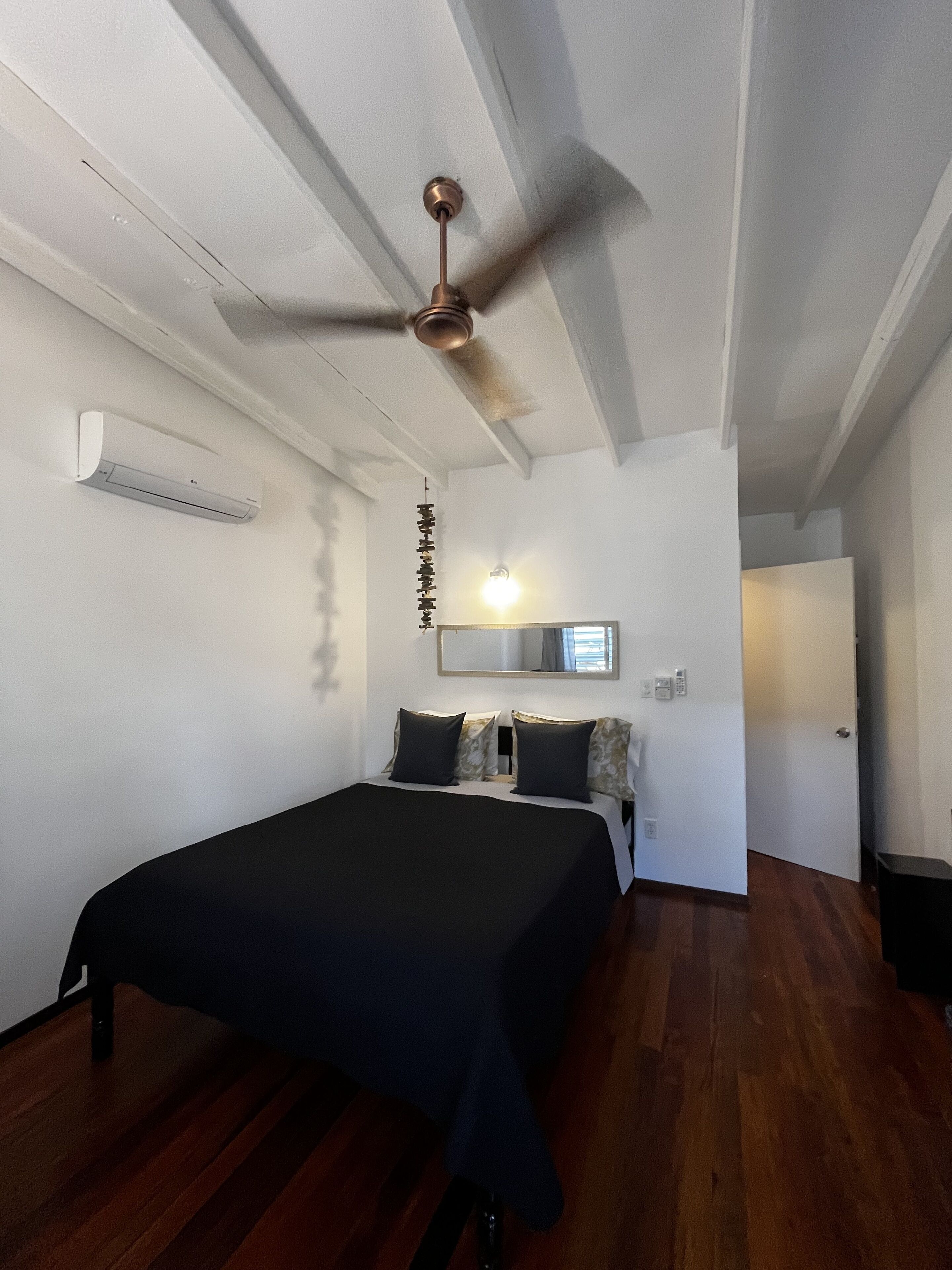 Een slaapkamer met een bed, een plafondventilator, een luchtverkoeler aan de muur en een spiegel.