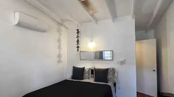 Een slaapkamer met een bed, een plafondventilator, een luchtverkoeler aan de muur en een spiegel.
