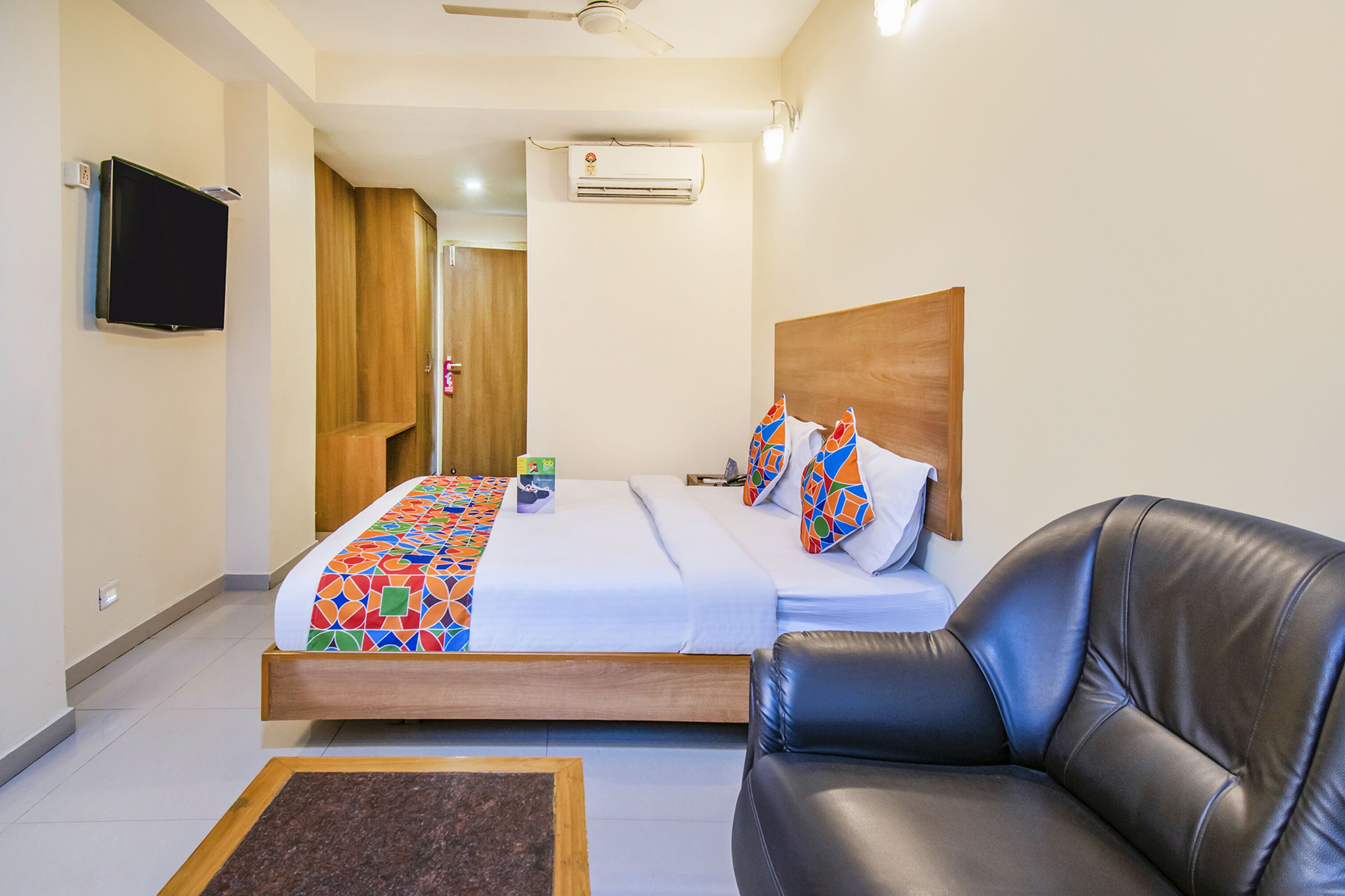 A hotel room with a bed, a leather sofa, a TV, and an air conditioning unit.