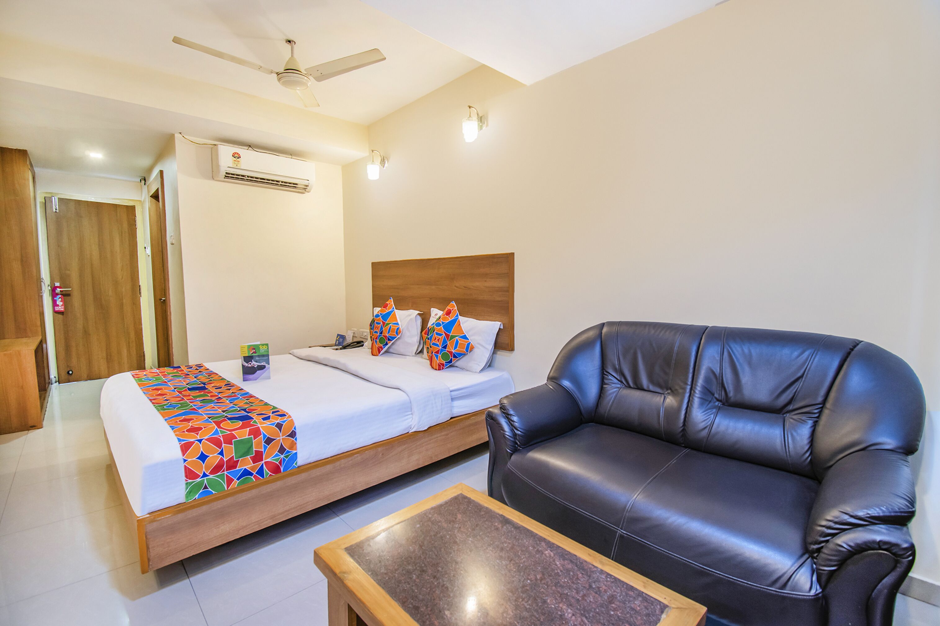 Une chambre d’hôtel comprenant un lit, un canapé en cuir noir, une table basse en bois, un appareil de climatisation et un ventilateur de plafond.