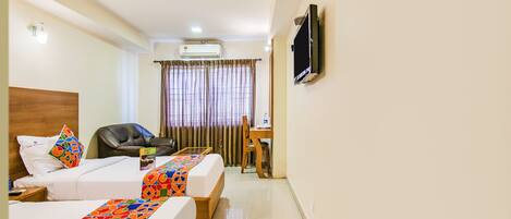 Habitación de hotel con dos camas, un escritorio, una silla, un televisor y un aire acondicionado.