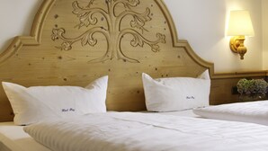 A hotel room with a wooden headboard featuring a carved tree design, two white pillows with "Hotel Boy" embroidered, and a bedside lamp. - Hotel Frey (Ismaning)