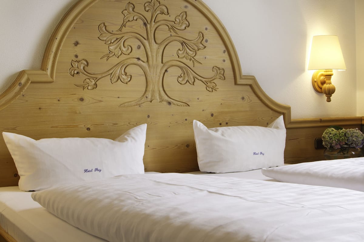 A hotel room with a wooden headboard featuring a carved tree design, two white pillows with "Hotel Boy" embroidered, and a bedside lamp.