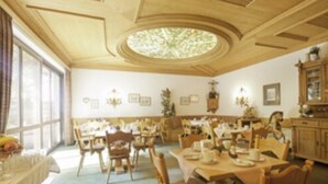 A dining area with round tables and chairs, a large window, and a chandelier. - Hotel Frey (Ismaning)