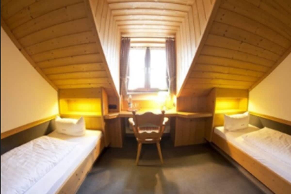 A small, cozy room with two single beds, a desk, and a chair.