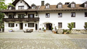 A traditional two-story building with a balcony, potted plants, and a cobblestone courtyard. - Hotel Frey (Ismaning)