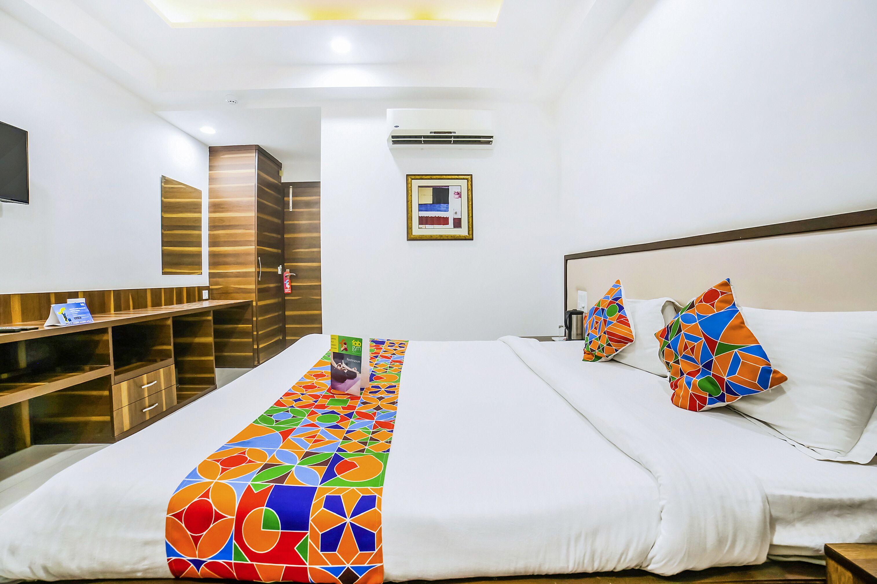 Habitación de hotel con una cama grande, un escritorio con silla, un televisor montado en la pared y un cuadro enmarcado.