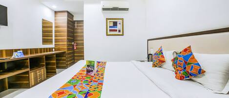 Habitación de hotel con una cama grande, un escritorio con silla, un televisor montado en la pared y un cuadro enmarcado.