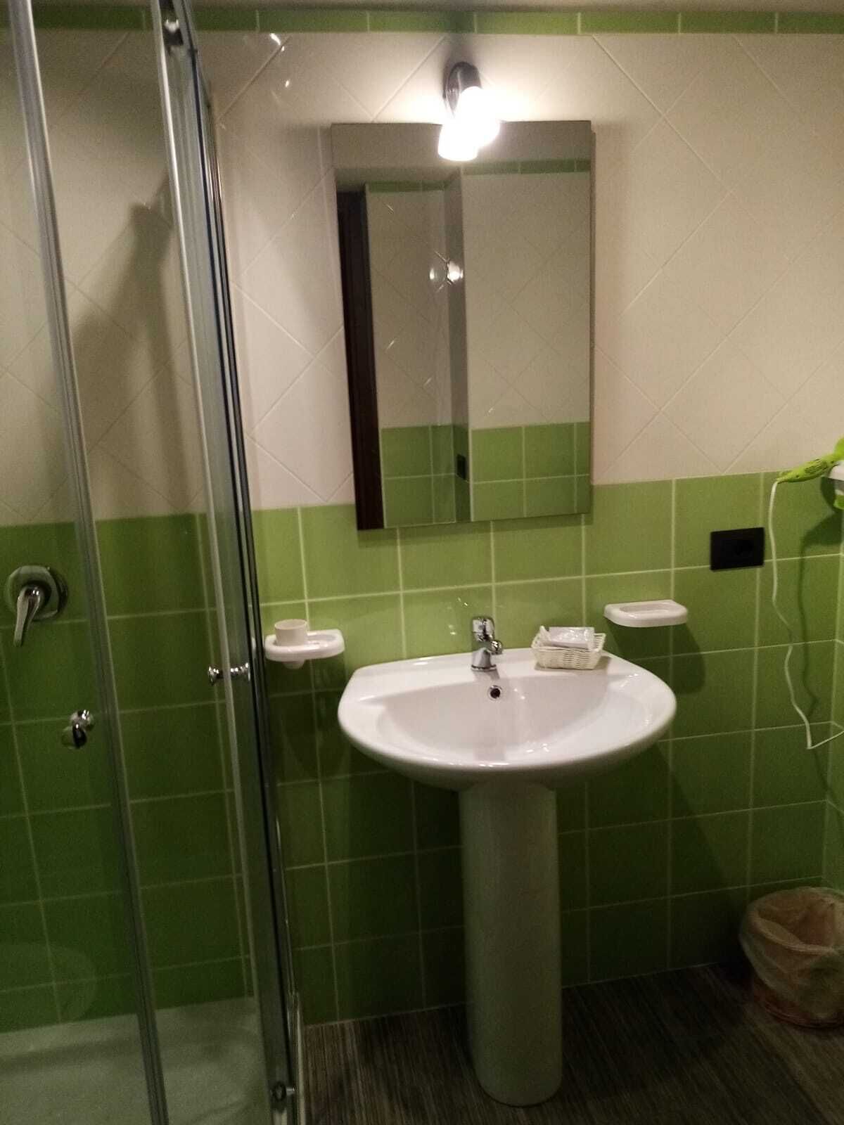 A bathroom with a glass shower enclosure, a white sink with a mirror above it, and green tiled walls.