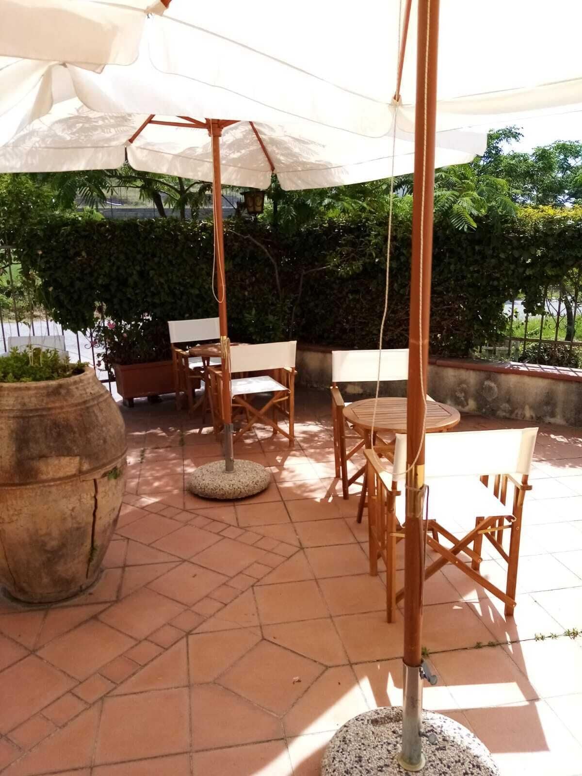 An outdoor patio with a round table and chairs, a large planter, and a pergola with a white canopy.