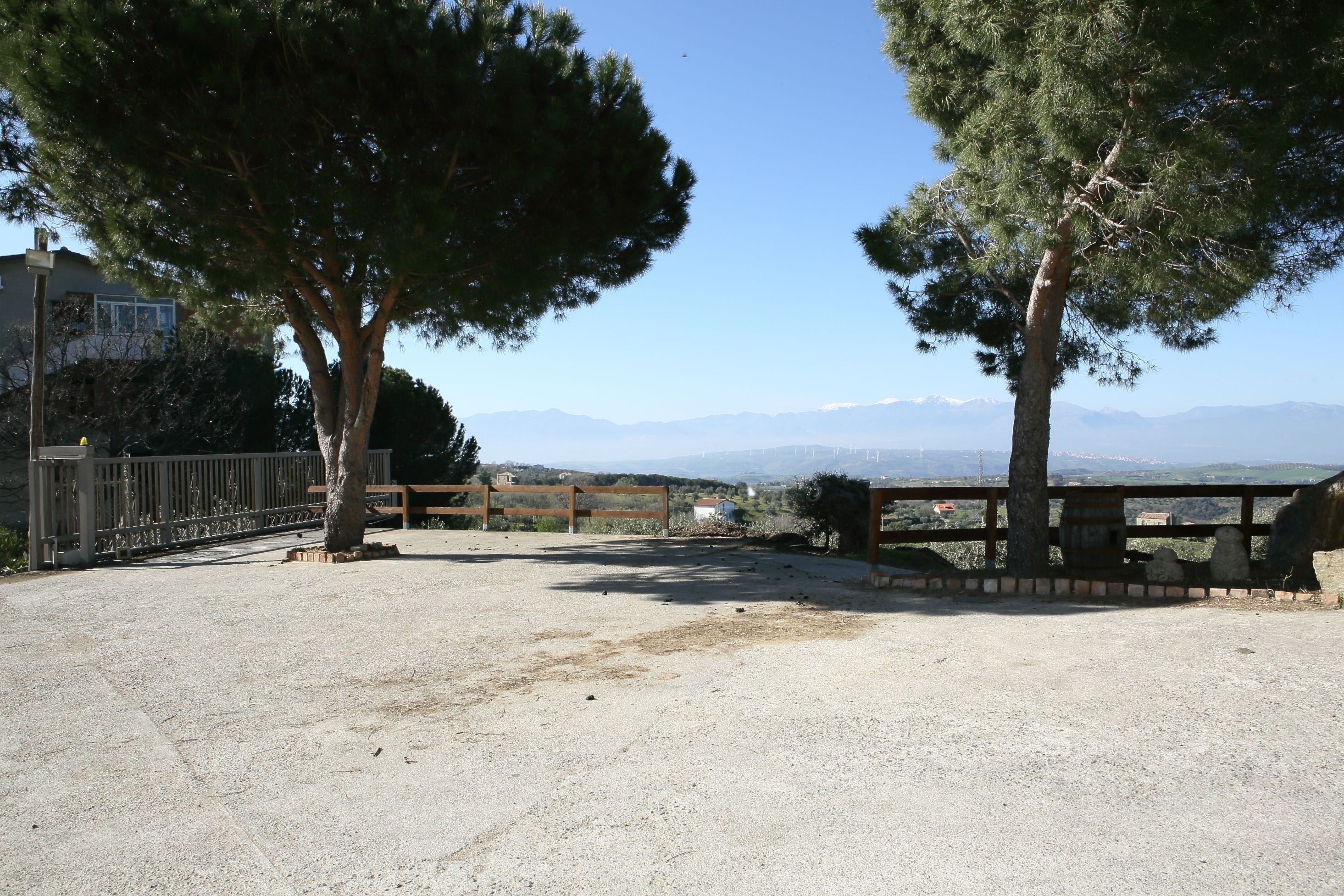 Un área pavimentada con cerca de madera y árboles, con vistas a un paisaje montañoso.
