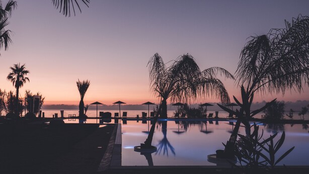 Ein ruhiger Blick auf den Pool im Abendrot, mit Liegestühlen und Sonnenschirmen.