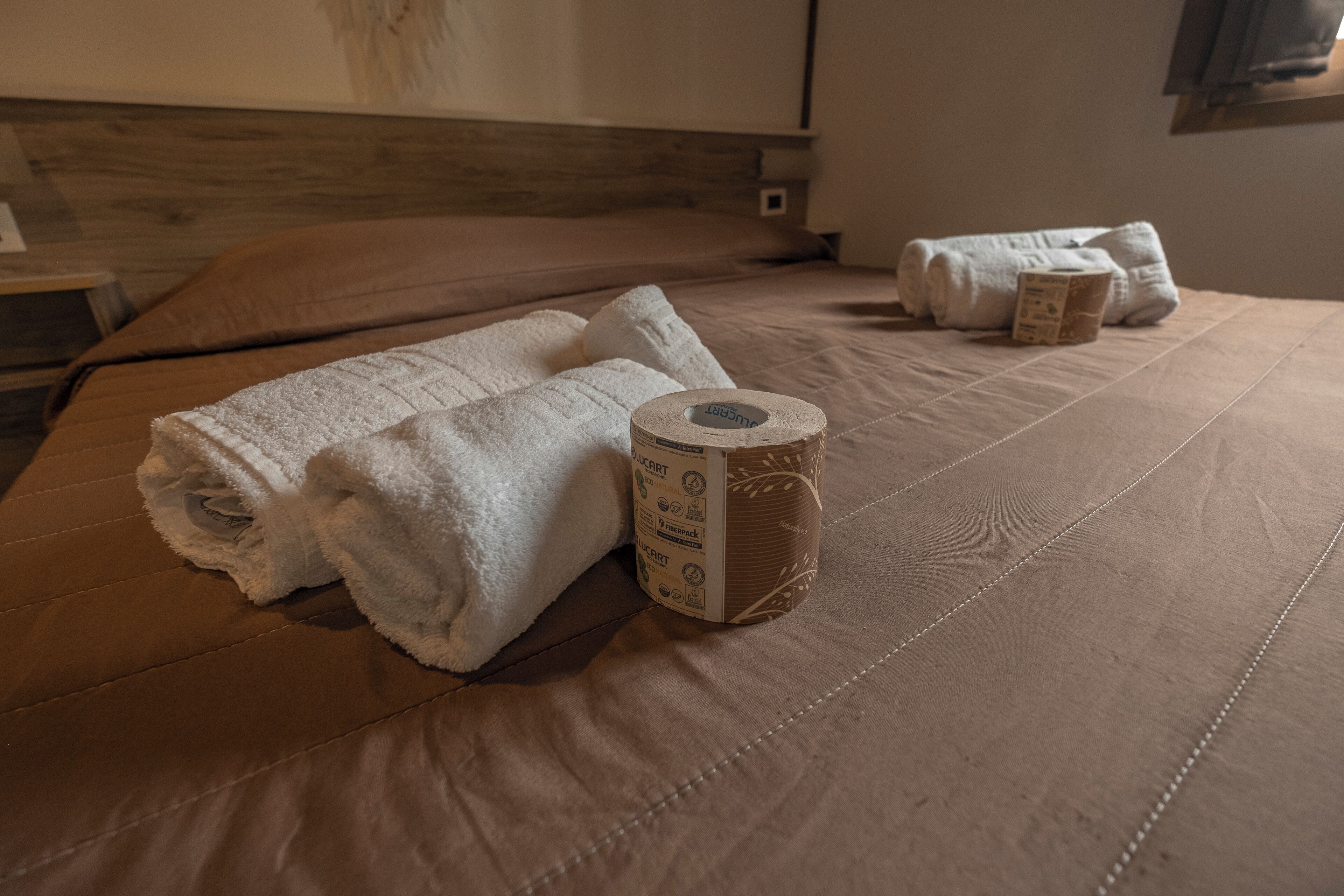 A neatly made bed with folded towels and a roll of toilet paper.