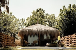 A thatched-roof structure with two wicker chairs and a table in front, surrounded by a wooden fence and lush greenery. - Riva del Sol Beach Resort (Santa Caterina dello Ionio)