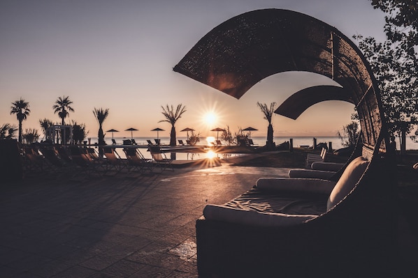 A beachside lounge area with sun loungers and umbrellas, overlooking the sea at sunset. - Riva del Sol Beach Resort (Santa Caterina dello Ionio)